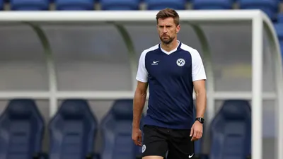 A photorealistic image of a 30-year-old male football coach with a stern expression, wearing a dark blue football jersey...
