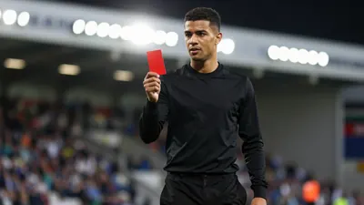 Floodlight rim light photograph of a young, anonymous, black-haired, black-shirted, black-pantsed Shamrock Rovers player...