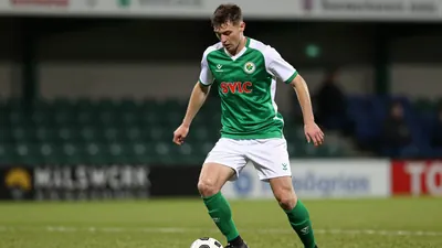A tight waist-up shot of a young, athletic-looking Shamrock Rovers player, wearing a green jersey with white sleeves and...